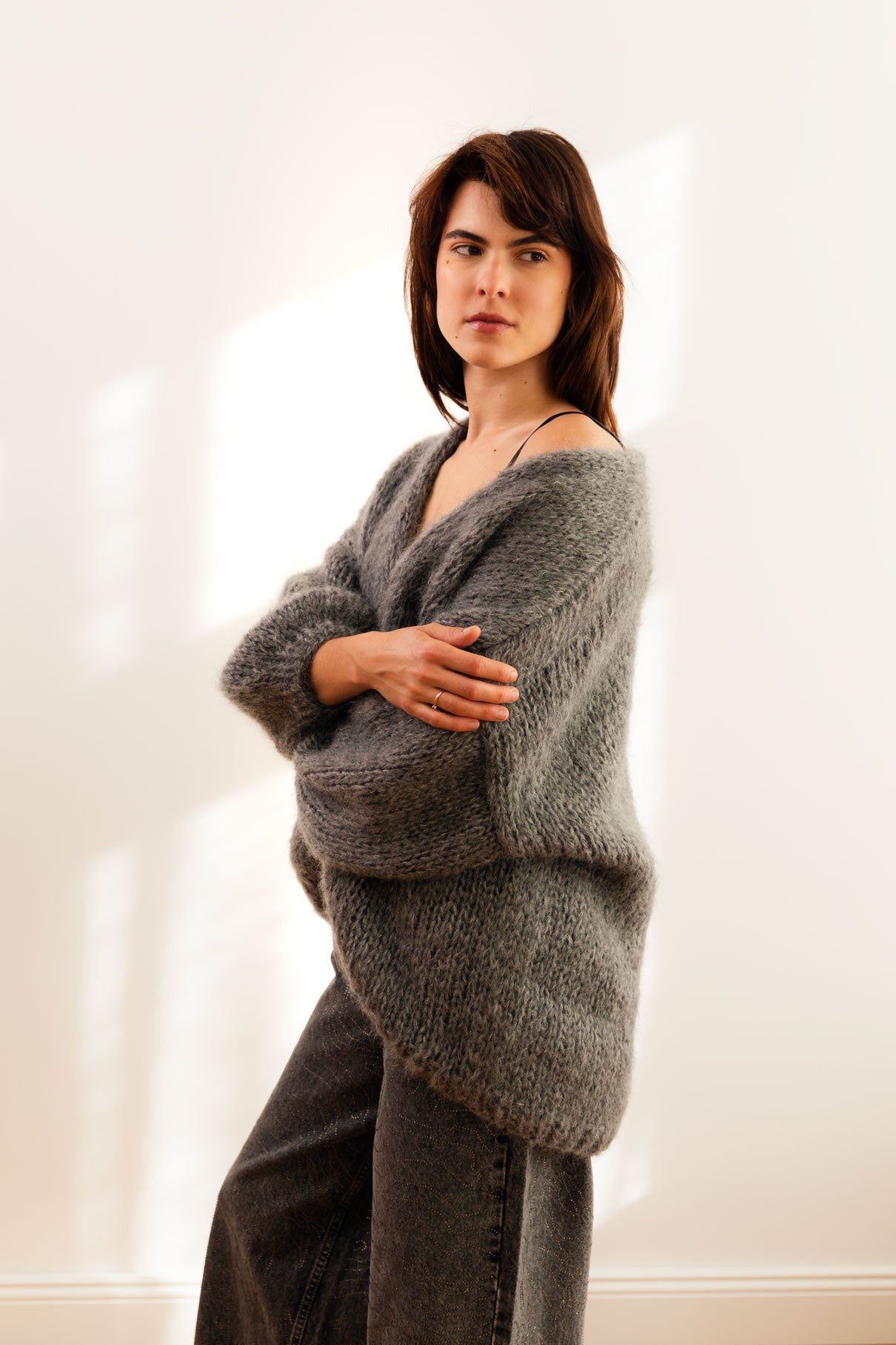 Woman wearing a grey mohair cardigan, paired with dark grey trouser, standing against a white background