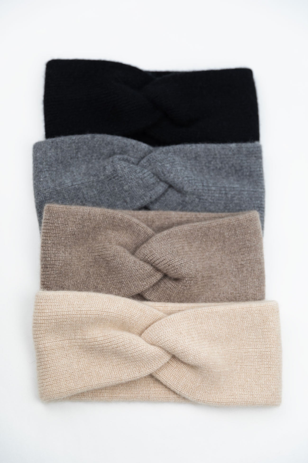 Flat lay of four 100% Mongolian cashmere twisted headbands in Black, Slate Grey, Taupe, and Oatmeal, showcasing the soft ribbed knit and front knot detail.