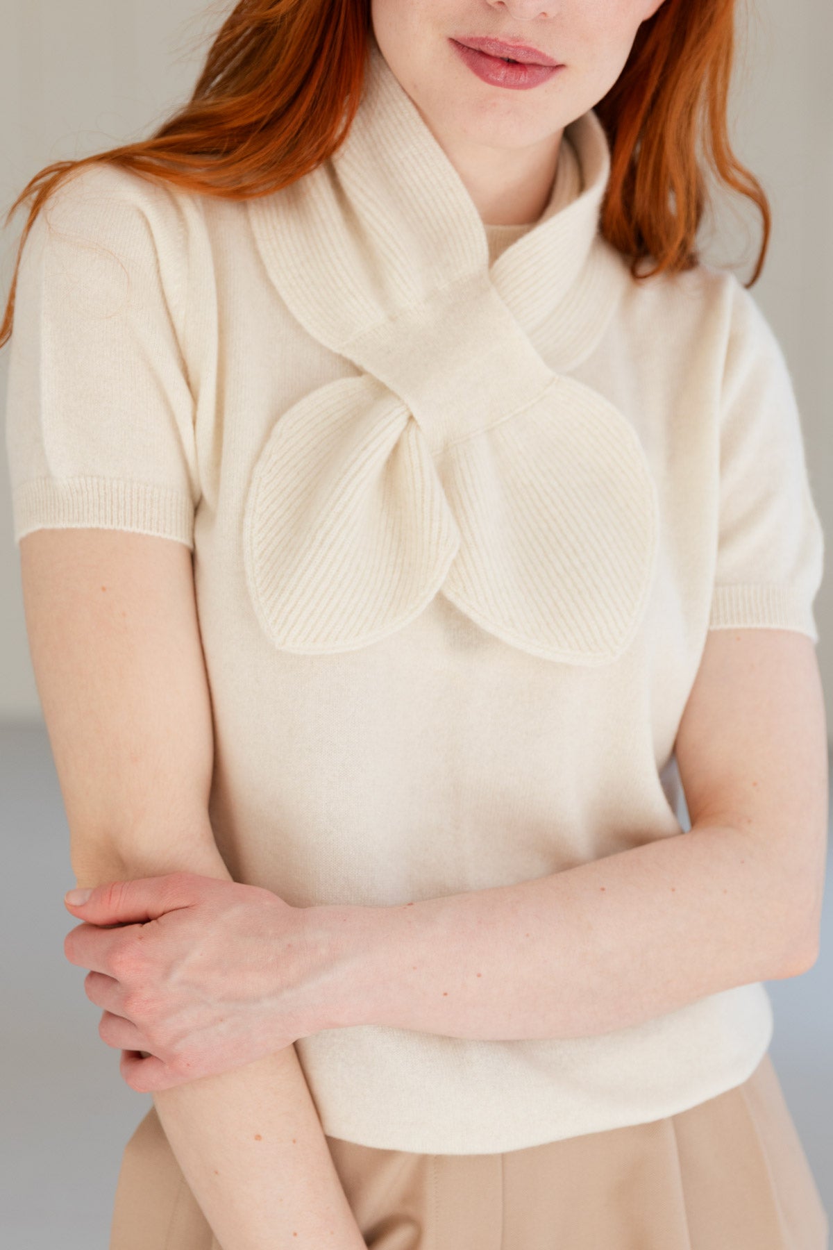 A close-up of a woman wearing a white cashmere mini scarf, paired with a white cashmere top.
