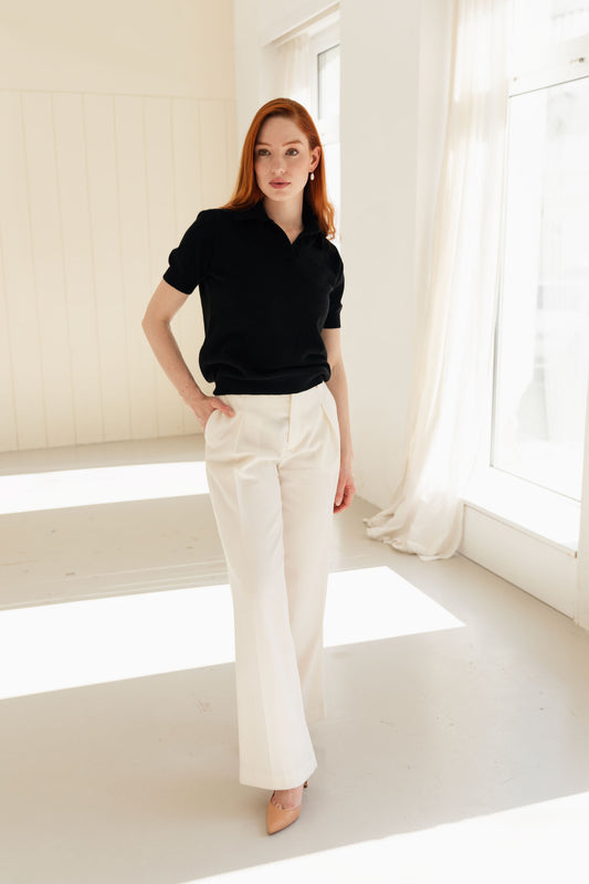 Woman wearing a 100% Mongolian cashmere polo shirt and white pants in a bright room with large windows.