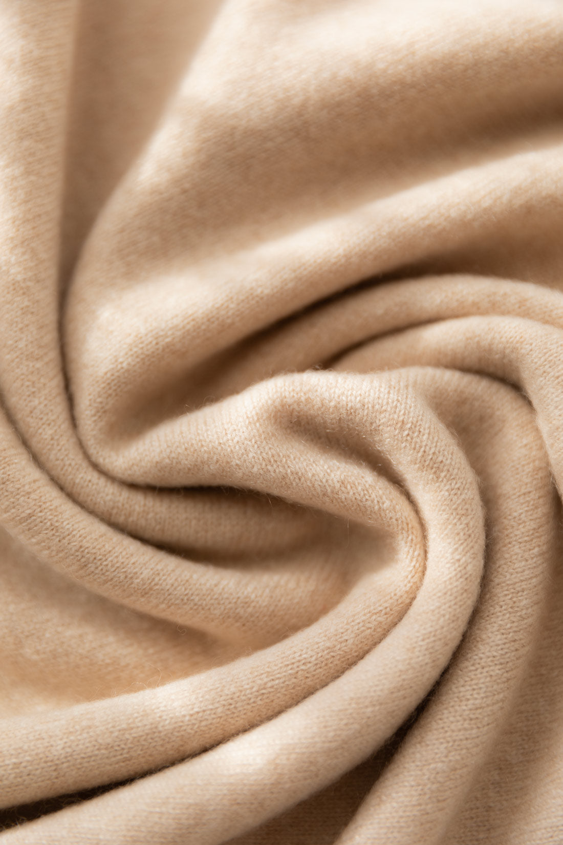A close-up of a beige cashmere fabric with soft folds and a smooth, slightly lustrous texture.