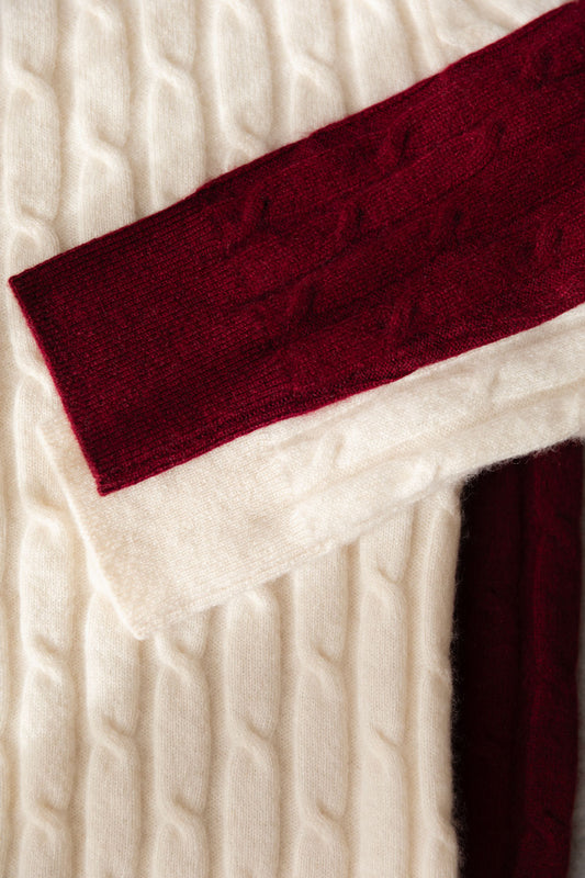 Close-up of two cable-knit cashmere sweaters in cream and dark burgundy layered over one side.