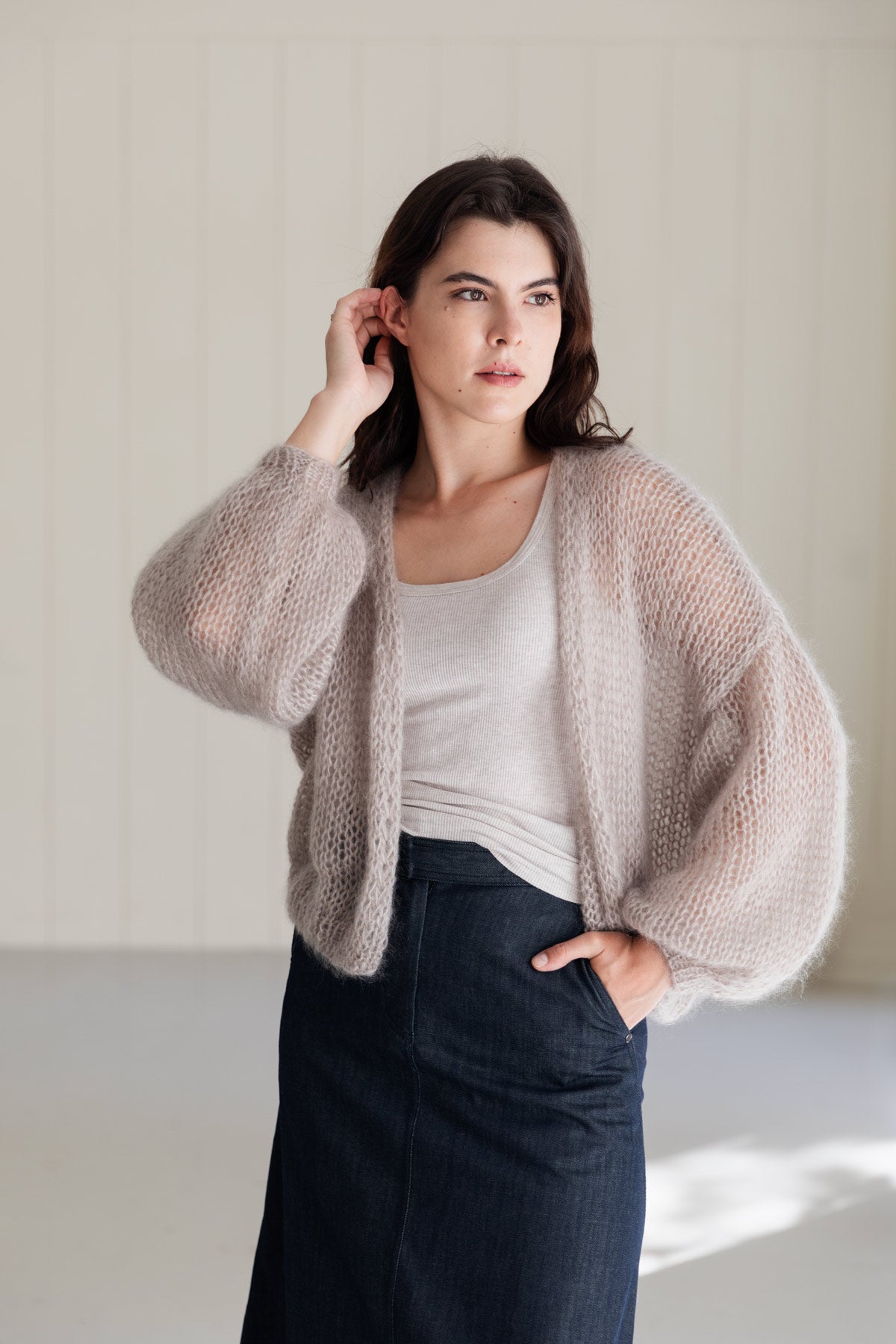 A woman wearing an airy beige mohair cardigan over a beige top, paired with a dark denim skirt.