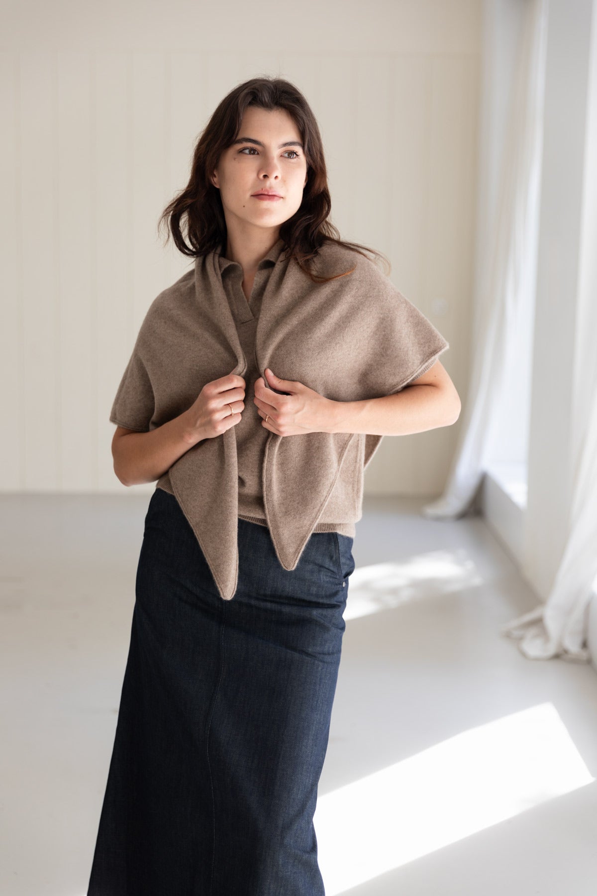 A woman wearing a cashmere triangle scarf in taupe over a brown top and a navy denim skirt.