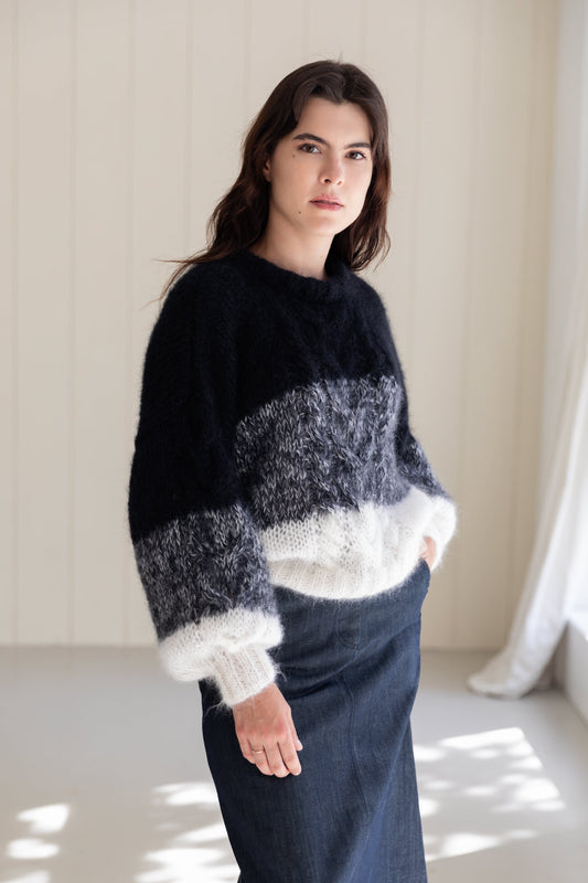 A woman wearing a mohair sweater with horizontal stripes in black, grey, and white, paired with a dark denim skirt.