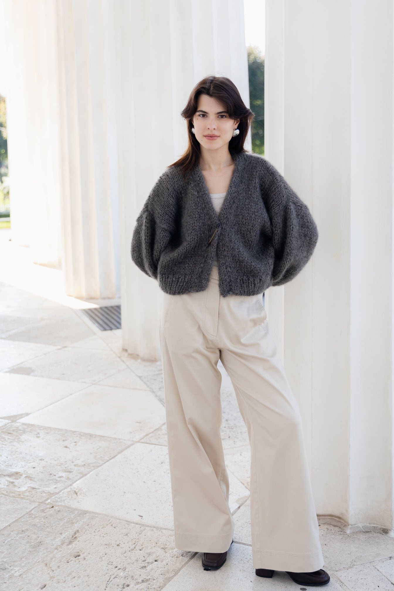 Woman wearing a dark gray cardigan and beige pants standing in front of white columns.