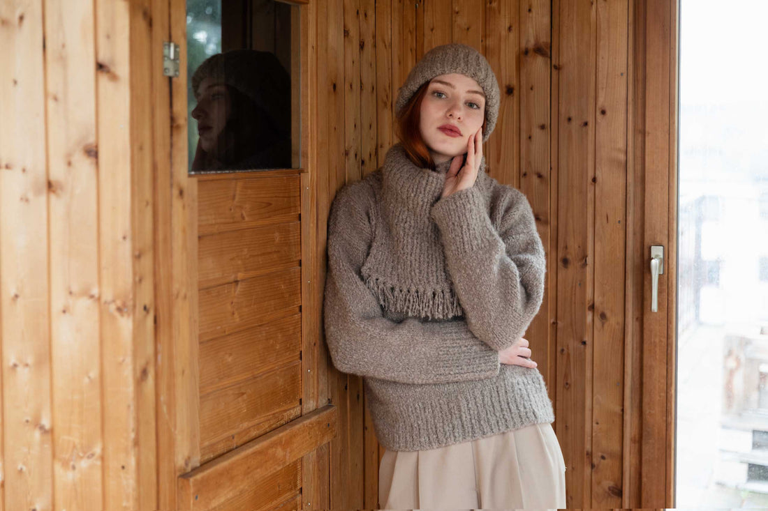 Woman wearing a cashmere set - beanie, neck-warmer and sweater on a wooden background
