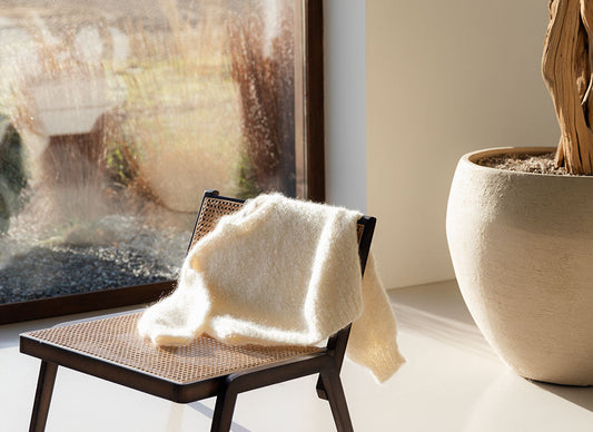 A white mohair sweater resting on a wooden chair near a big window