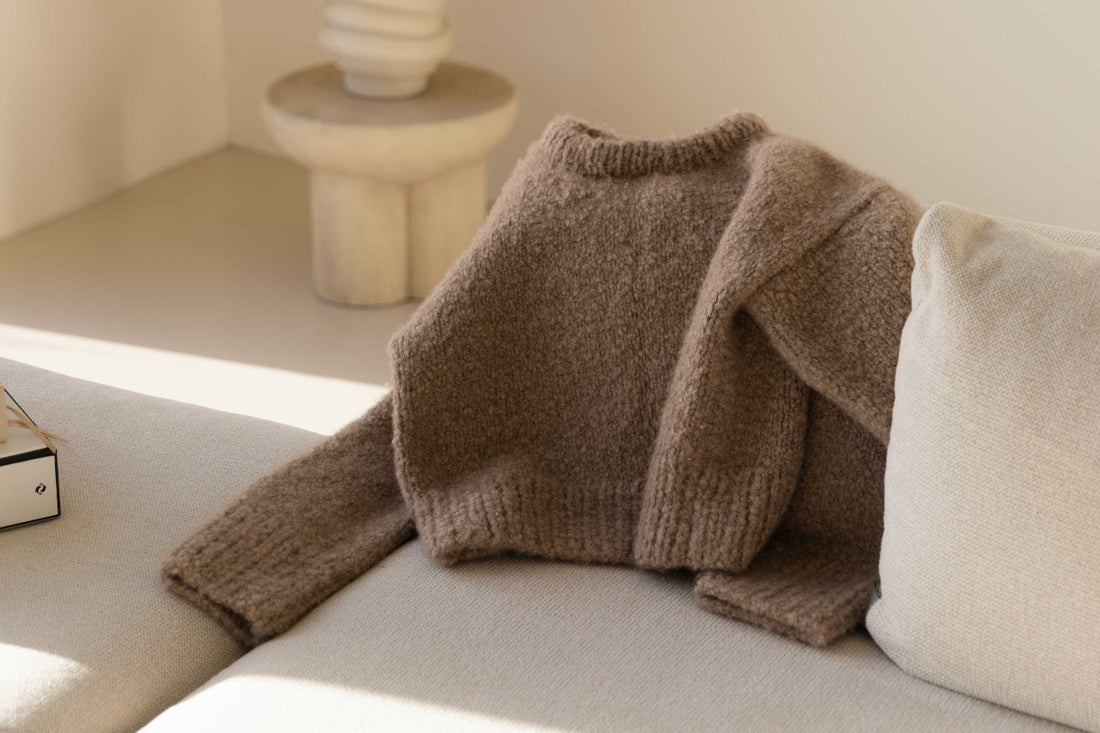 Minimalist interior with a bouclé cashmere sweater resting on a white sofa