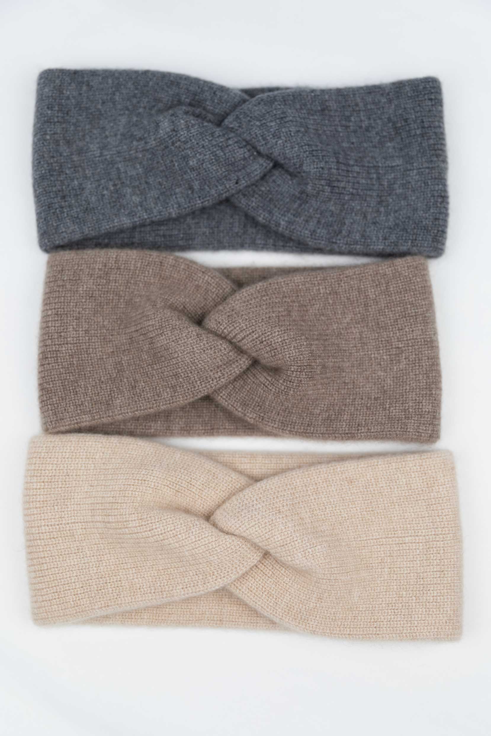 Flat lay of three 100% Mongolian cashmere twisted headbands in Slate Grey, Taupe, and Oatmeal, showcasing the soft ribbed knit and front knot detail.