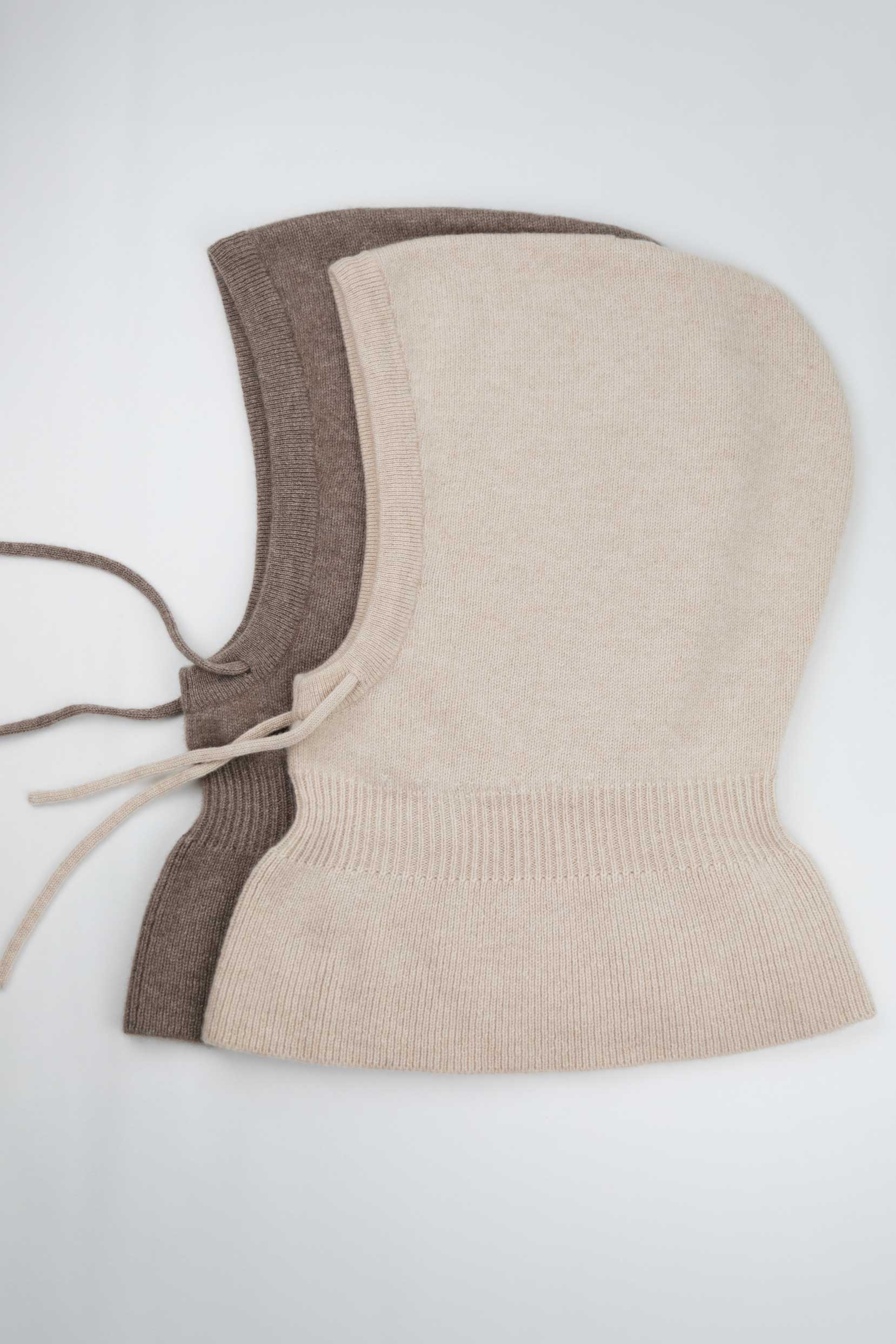 Side view of two 100% Mongolian cashmere balaclavas in beige and brown, showing the adjustable drawstring and wide shoulder drape.