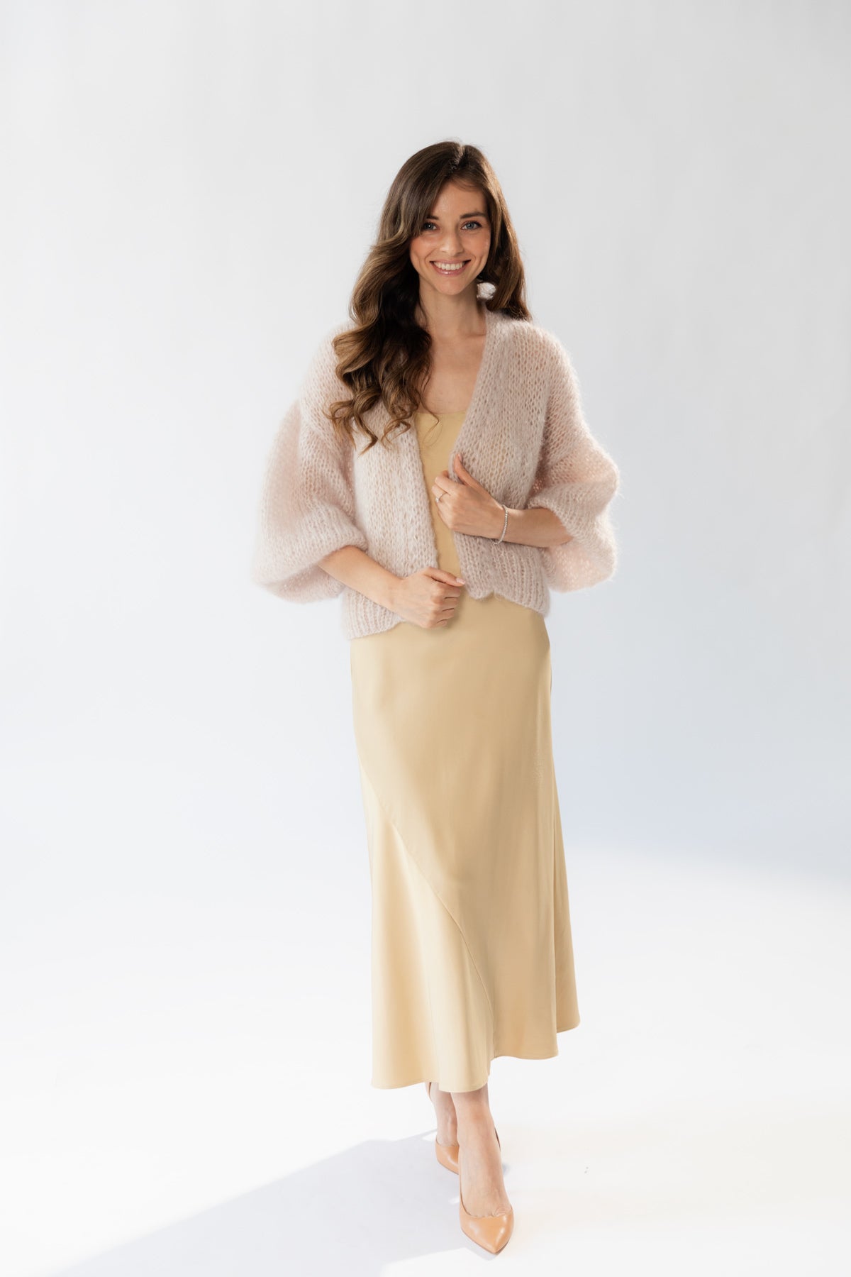 A woman wearing a silk beige midi dress paired with an elegant mohair cardigan and nude heels.