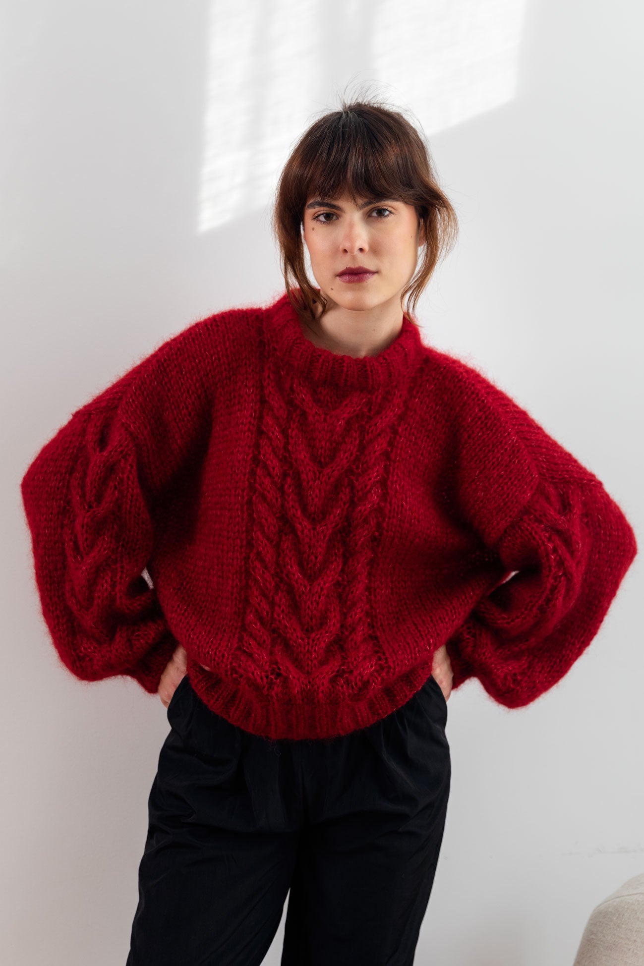 Woman wearing a burgundy-red mohair sweater, paired with black bottoms, standing against a white background