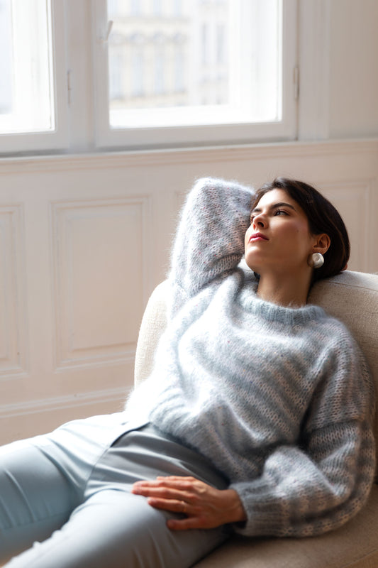 Woman wearing a striped mohair sweater in blue and white, sitting on a sofa