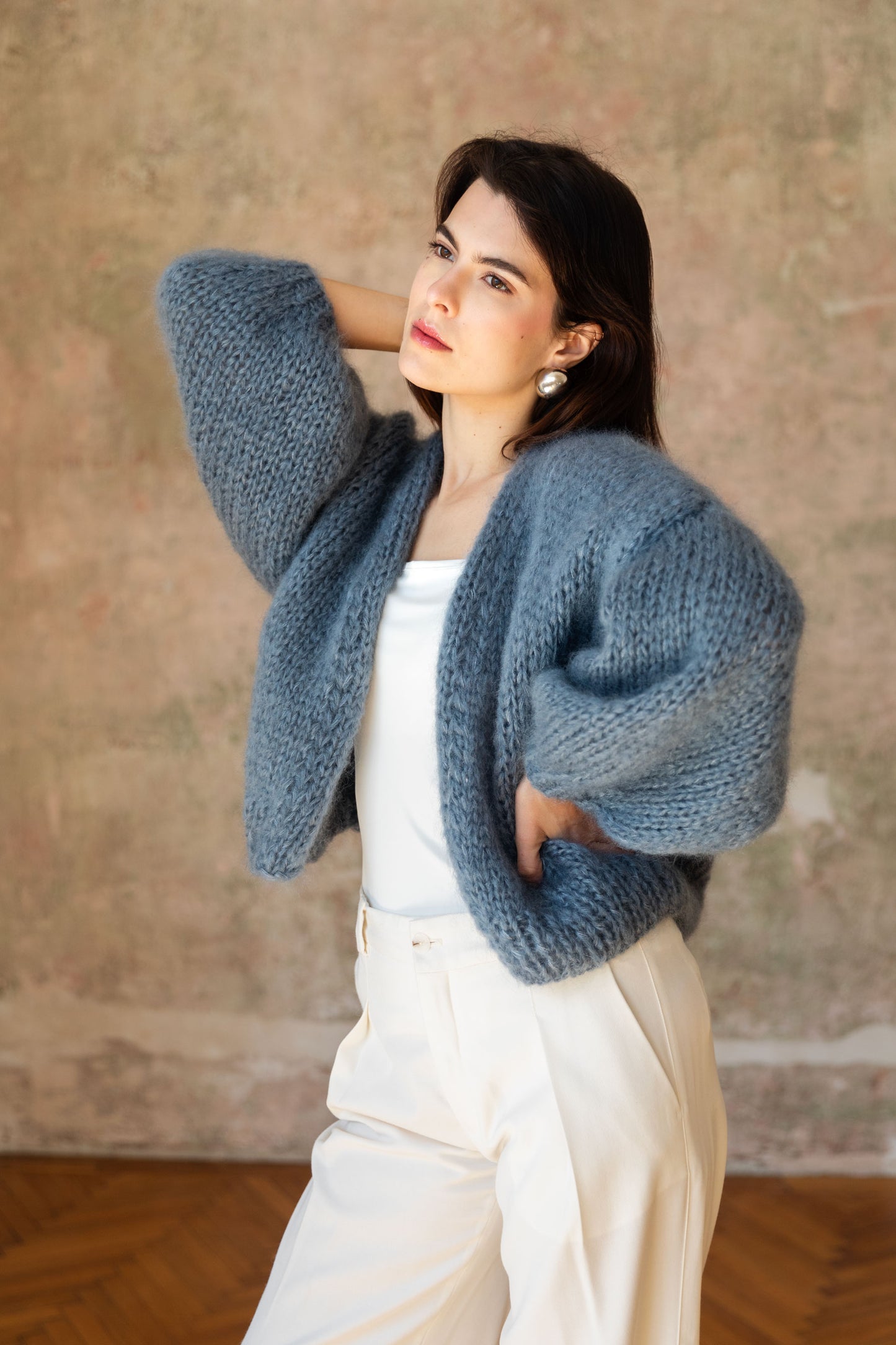 Woman wearing a blue mohair cardigan over a white top and trousers.