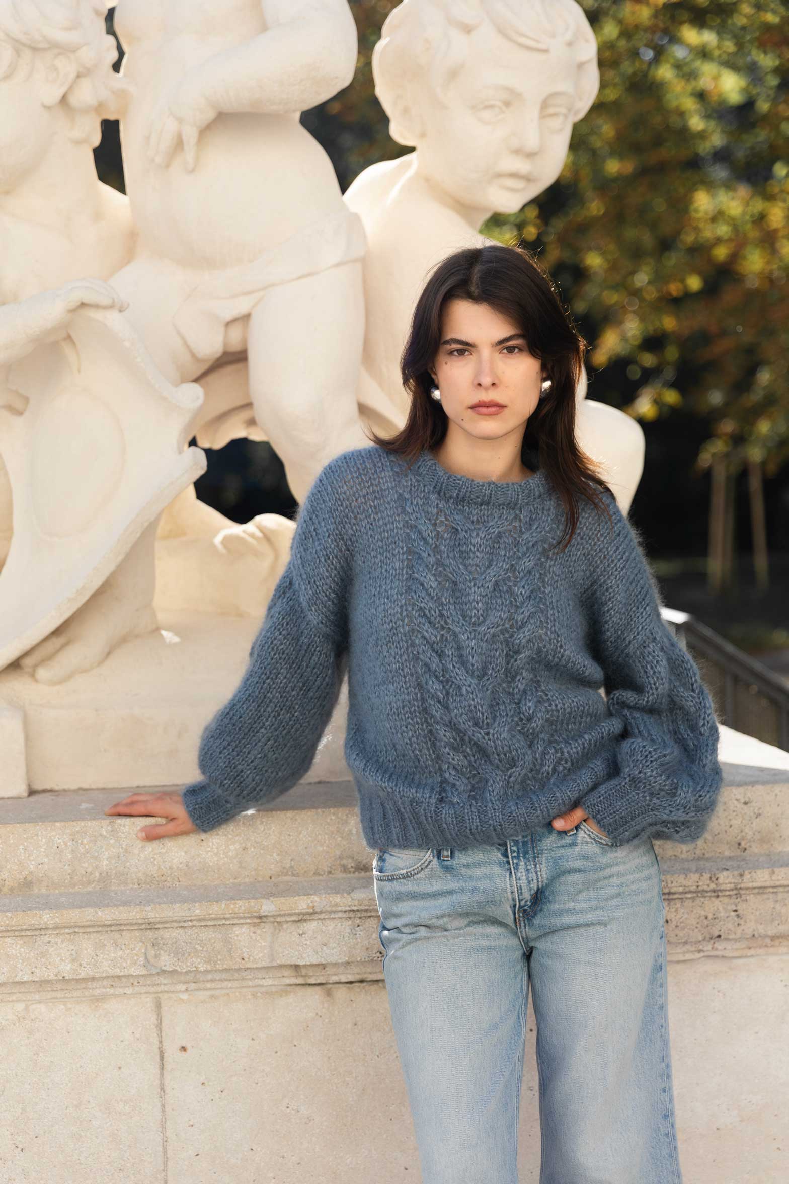 Woman wearing a blue mohair sweater standing in front of classical statues.
