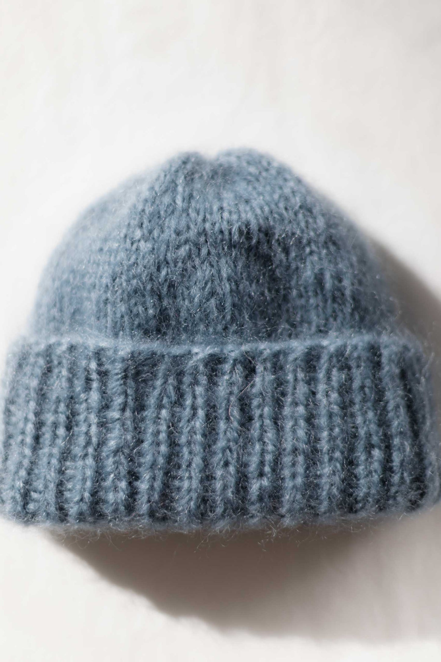 A dusty blue mohair beanie hat with a ribbed cuff, photographed against a plain off-white background.