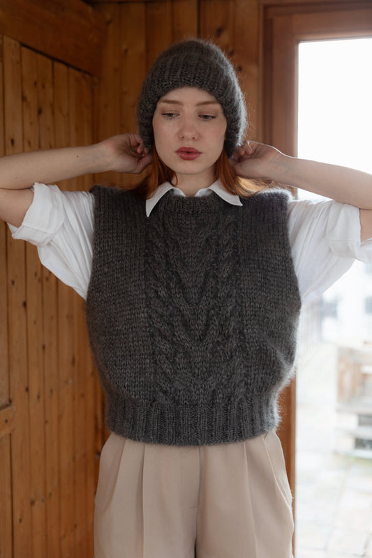 Woman wearing a chunky mohair beanie and a matching mohair vest, over a white shirt and beige elegant trousers.