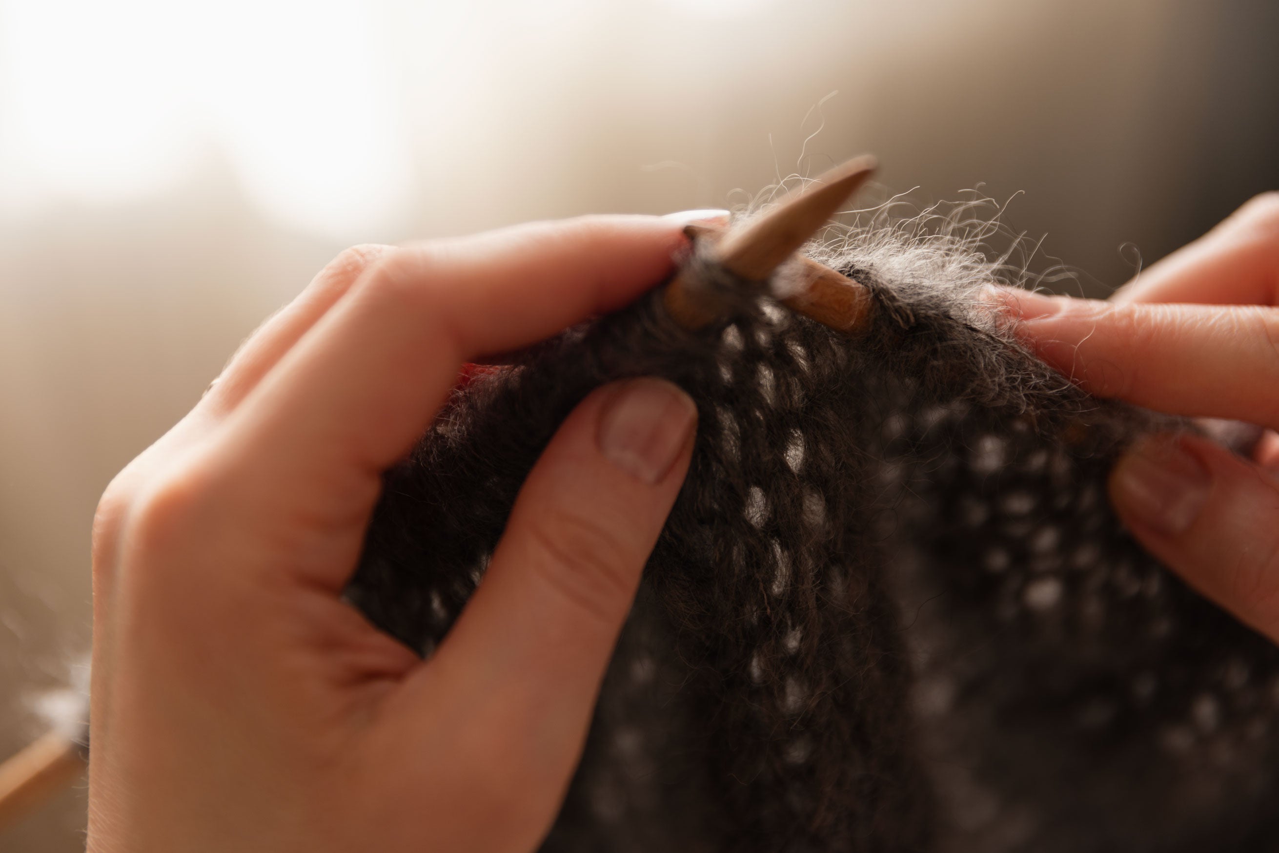 Close-up of hands knitting with mohair yarn and wooden needles.