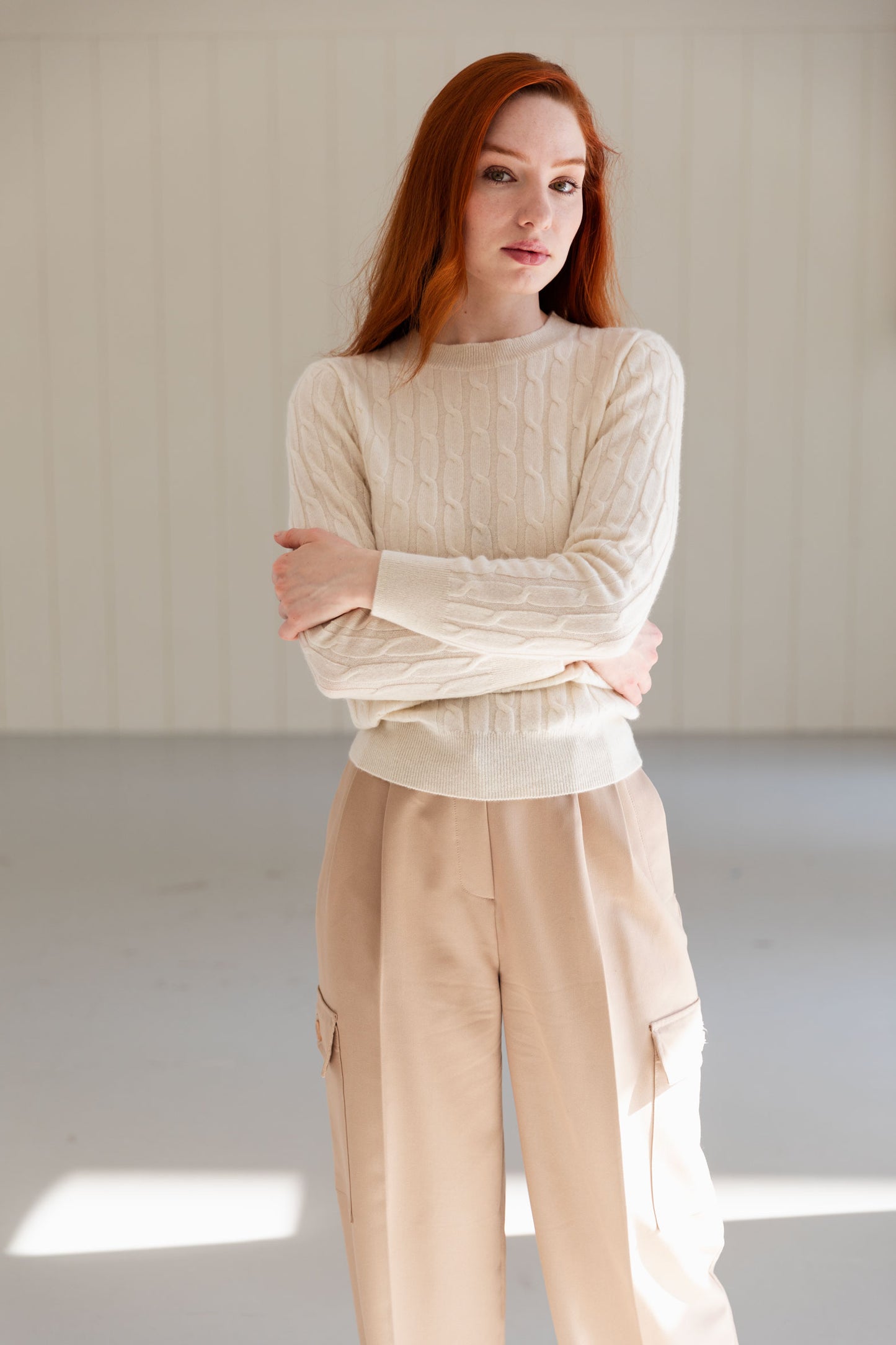 Woman wearing a white cable knit cashmere sweater and beige trousers