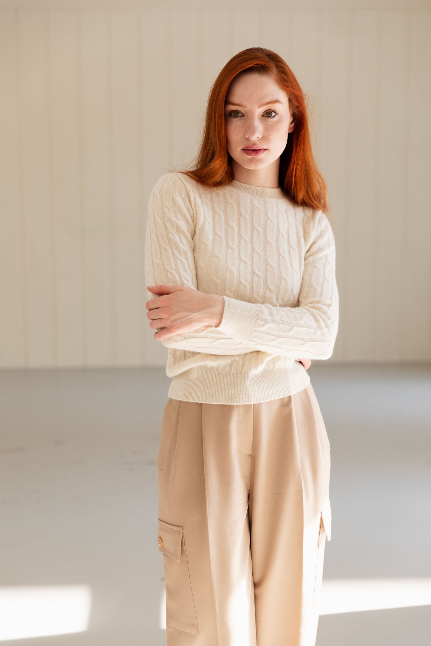 Woman wearing a white cable knit cashmere sweater and beige pants