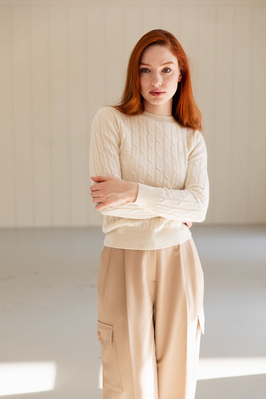 Woman wearing a white cable knit cashmere sweater and beige pants