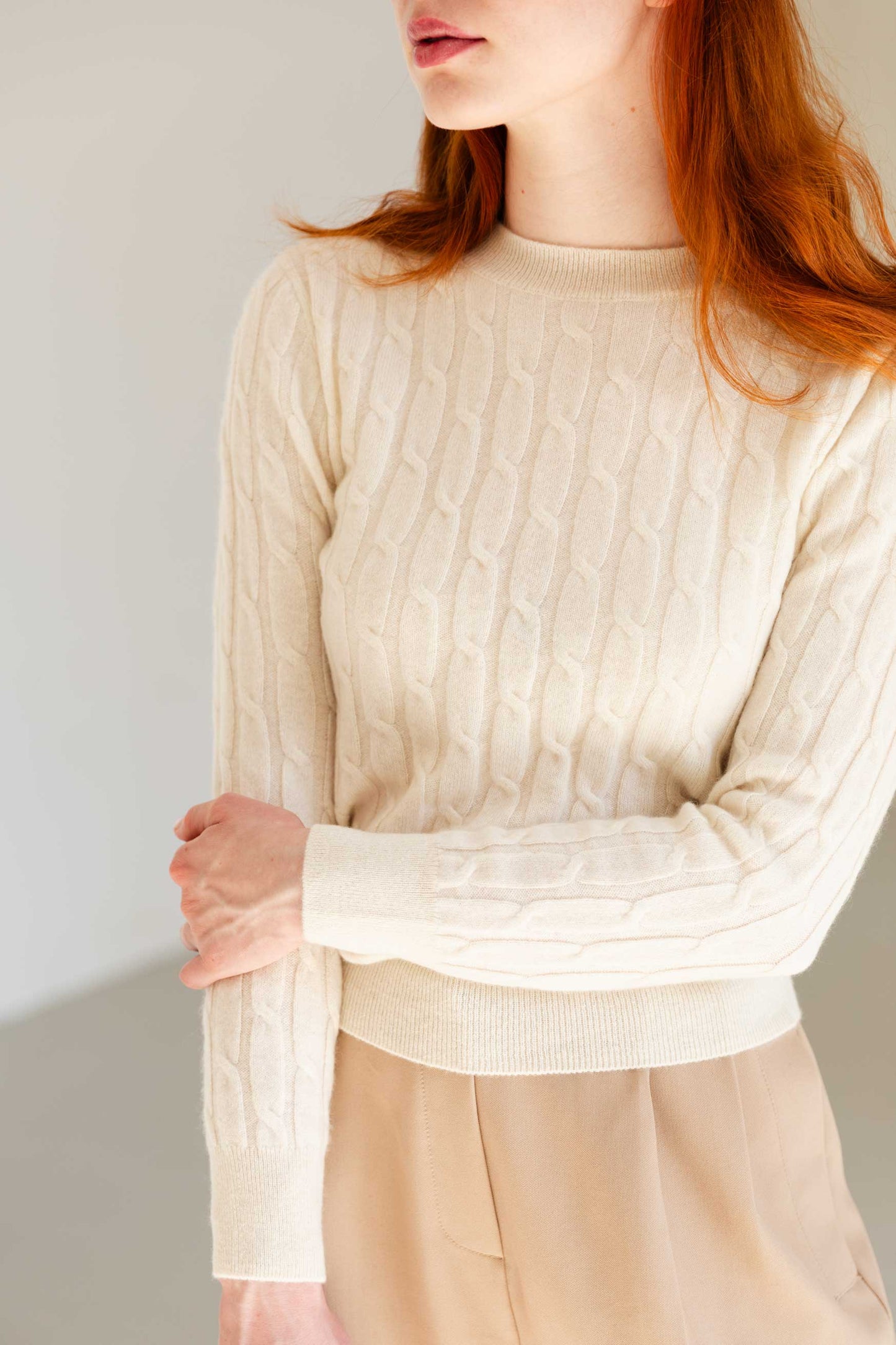 A close up of a woman wearing a white cable knit cashmere sweater