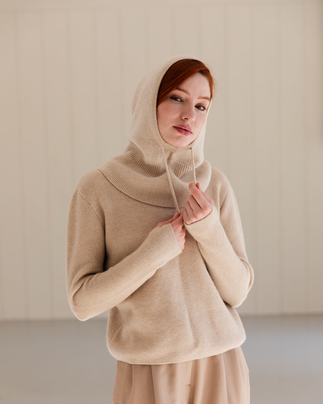 Woman wearing a beige cashmere balaclava, paired with a matching cashmere sweater.