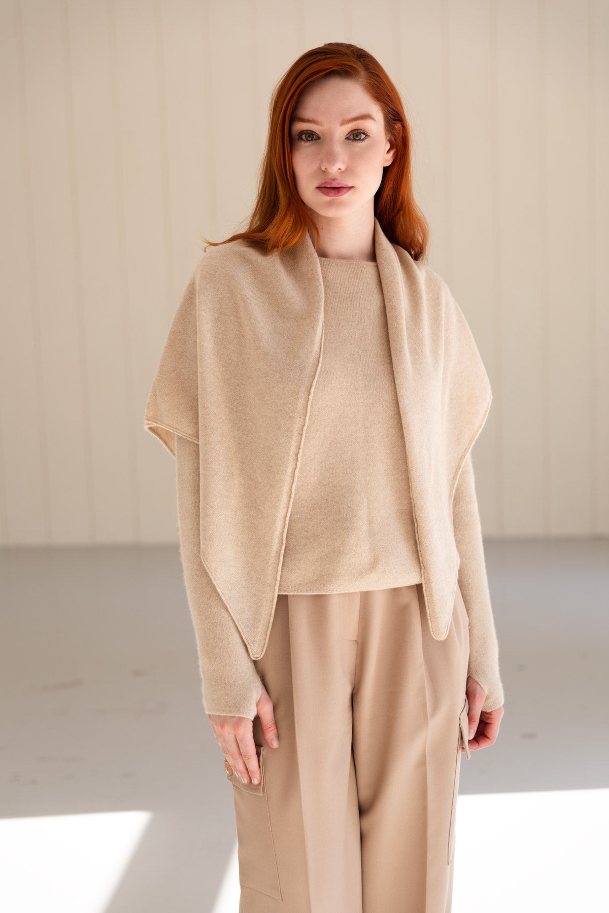 A woman with red hair wearing a beige cashmere sweater, and matching triangle scarf.