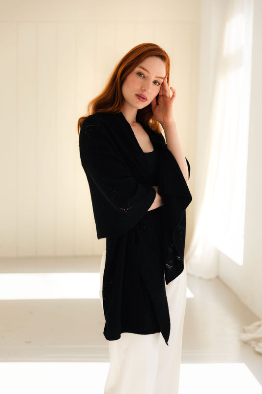 Woman wearing a black cashmere shawl in a bright, minimalistic room.