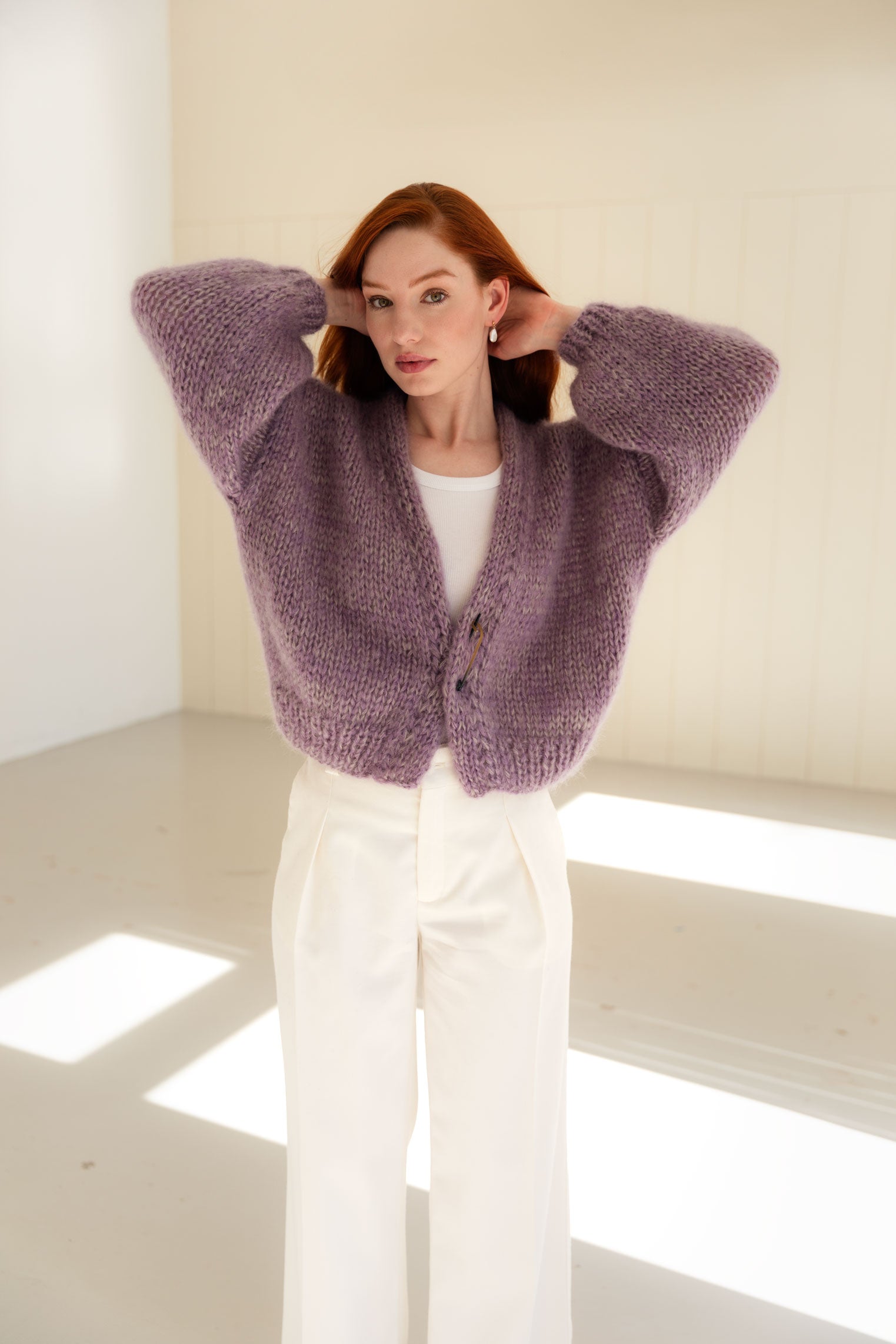 Woman wearing a purple mohair cardigan in a minimal white room