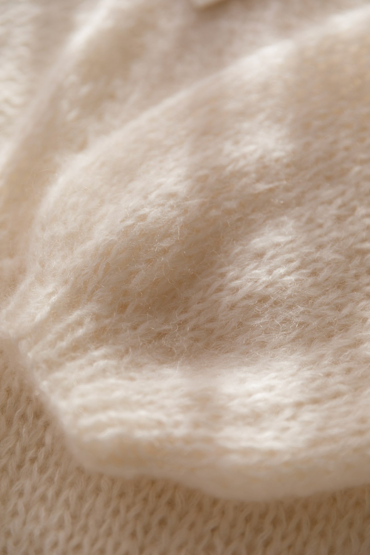 Close-up of a soft, cream-colored mohair knit fabric with a fuzzy, plush texture.
