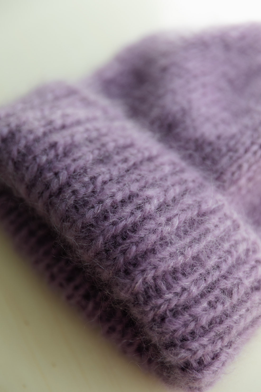 A close-up of a soft, fuzzy mohair beanie in a muted lavender-purple colour, showing the detailed knit texture.