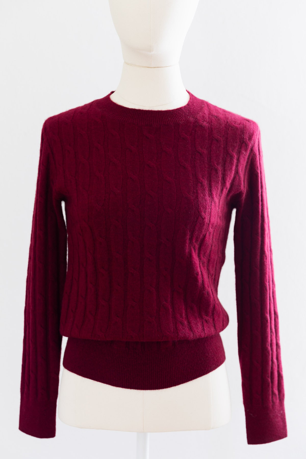 A dark cherry cable-knit cashmere sweater displayed on a cream mannequin torso.