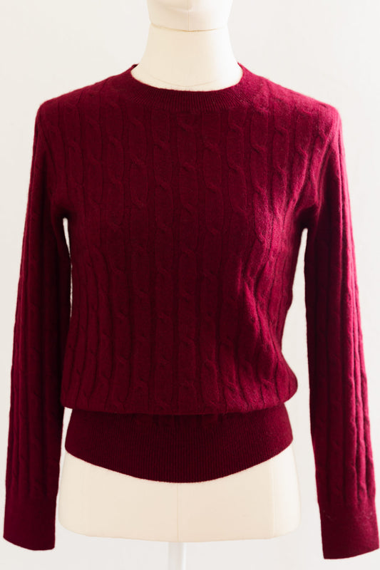 A dark burgundy cable-knit cashmere sweater displayed on a cream mannequin torso against a plain white background.