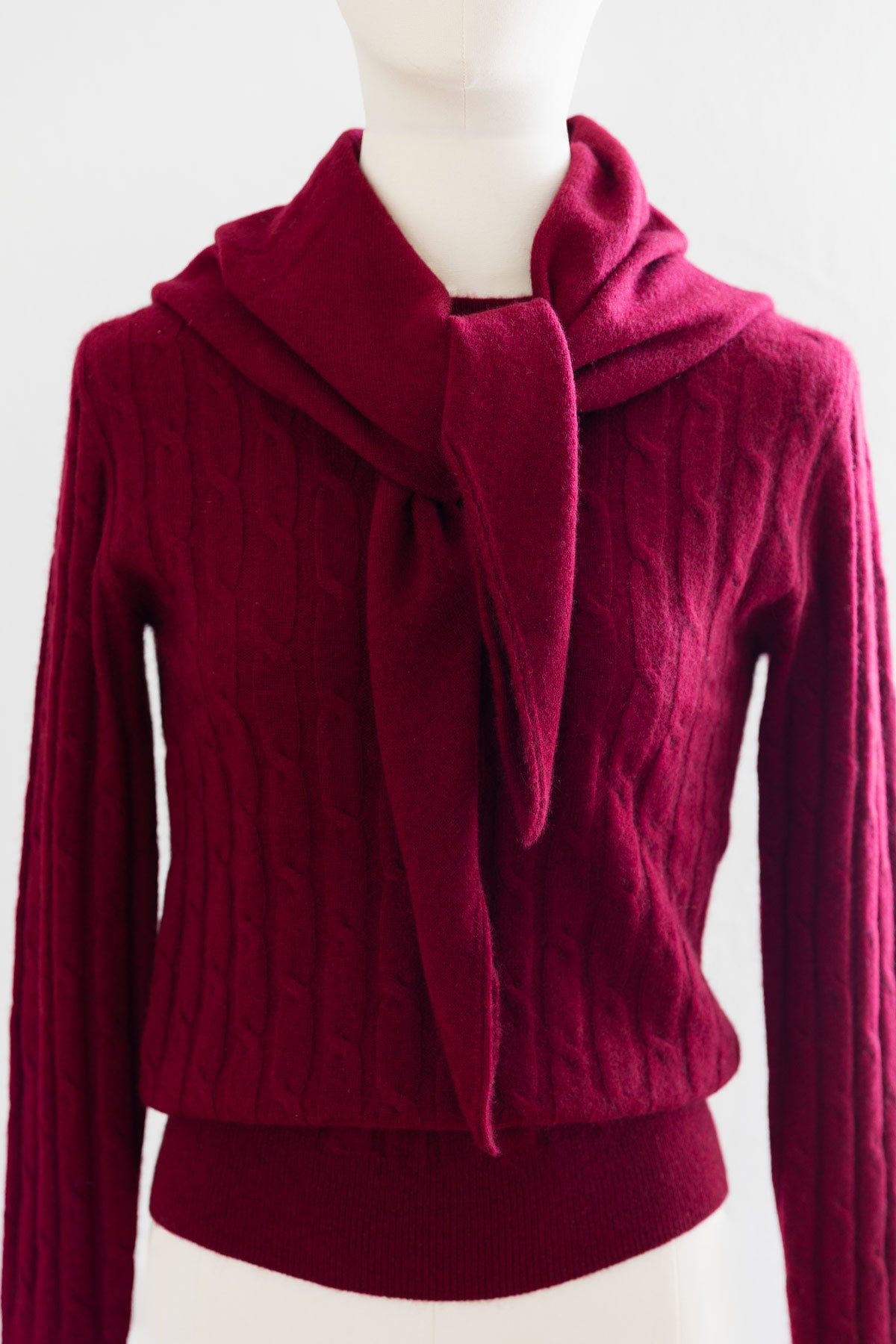 A deep burgundy cashmere sweater with a matching triangle scarf tied around the neck, displayed on a white mannequin.