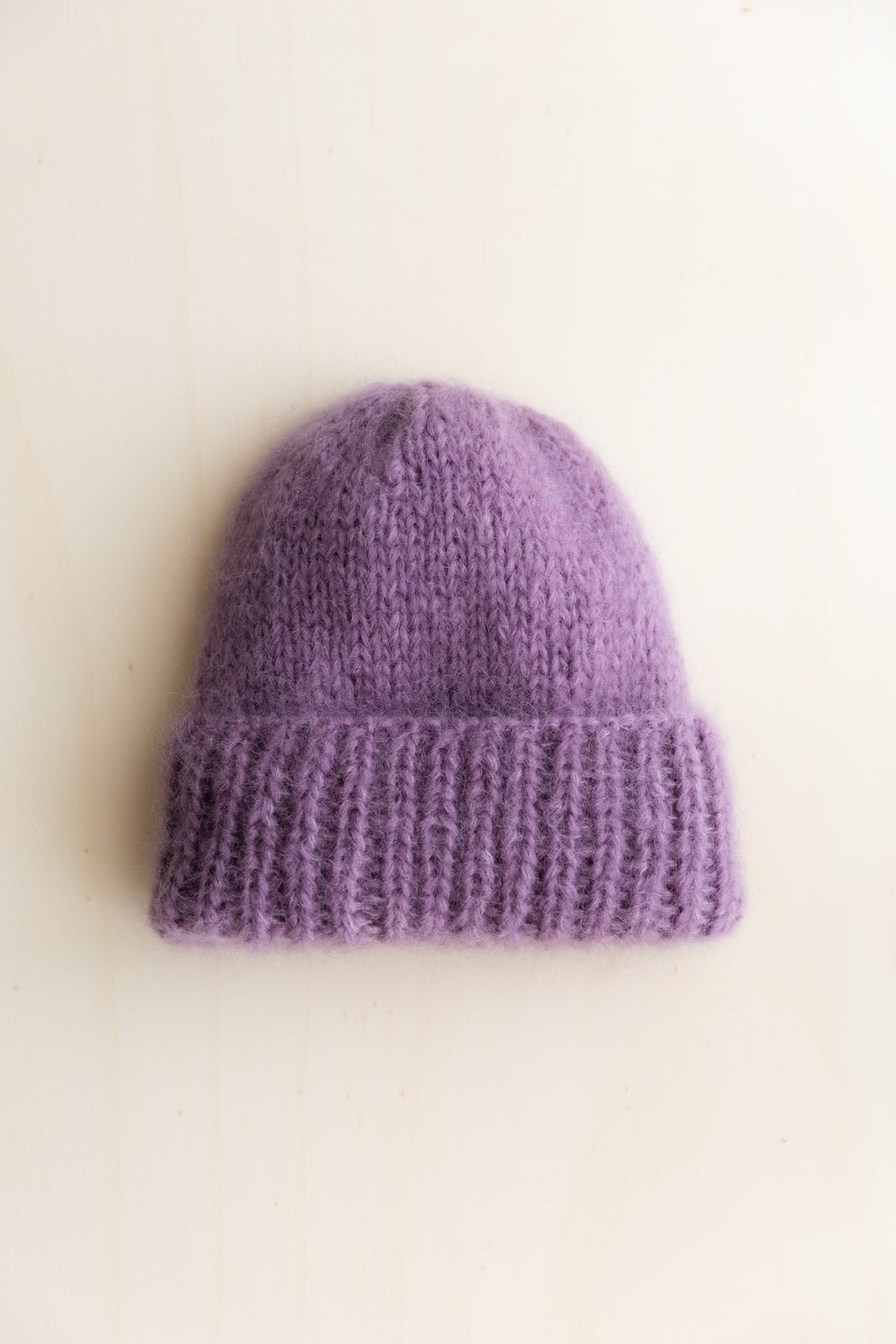 A soft lavender purple mohair beanie hat with a ribbed cuff, photographed flat against a light cream background.