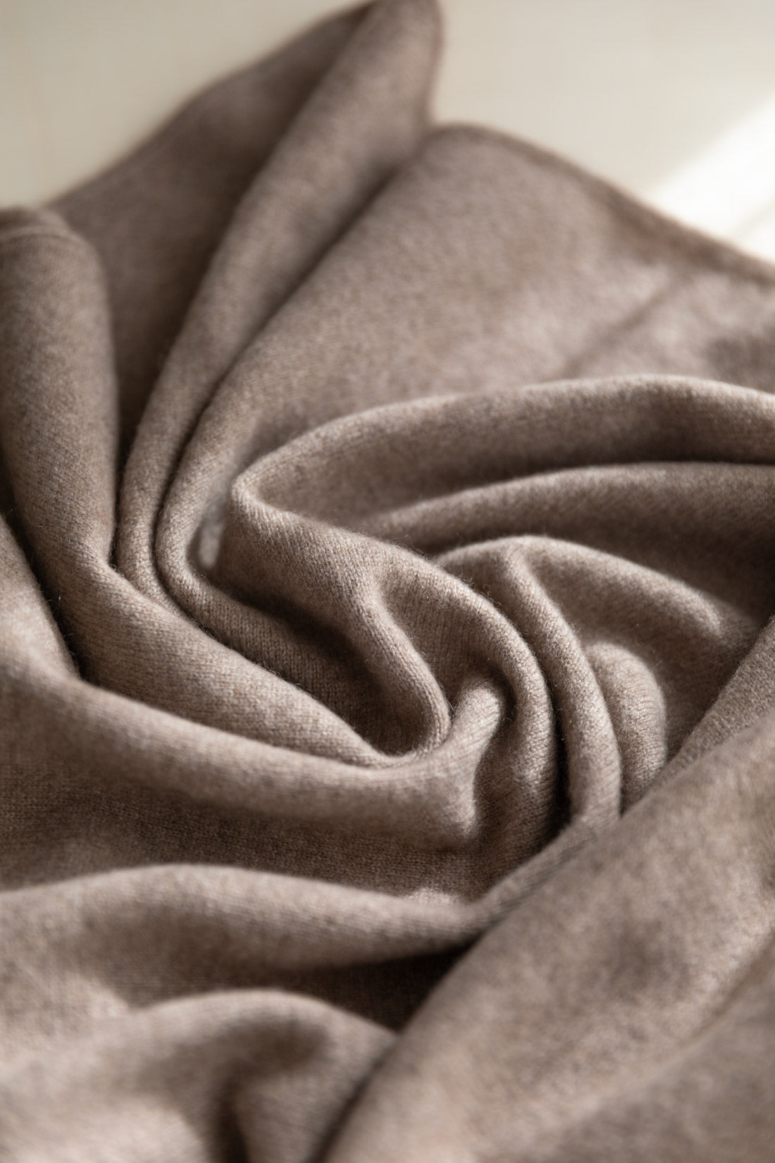 A close-up of draped taupe-brown cashmere fabric, with a textured, brushed surface and elegant folds.