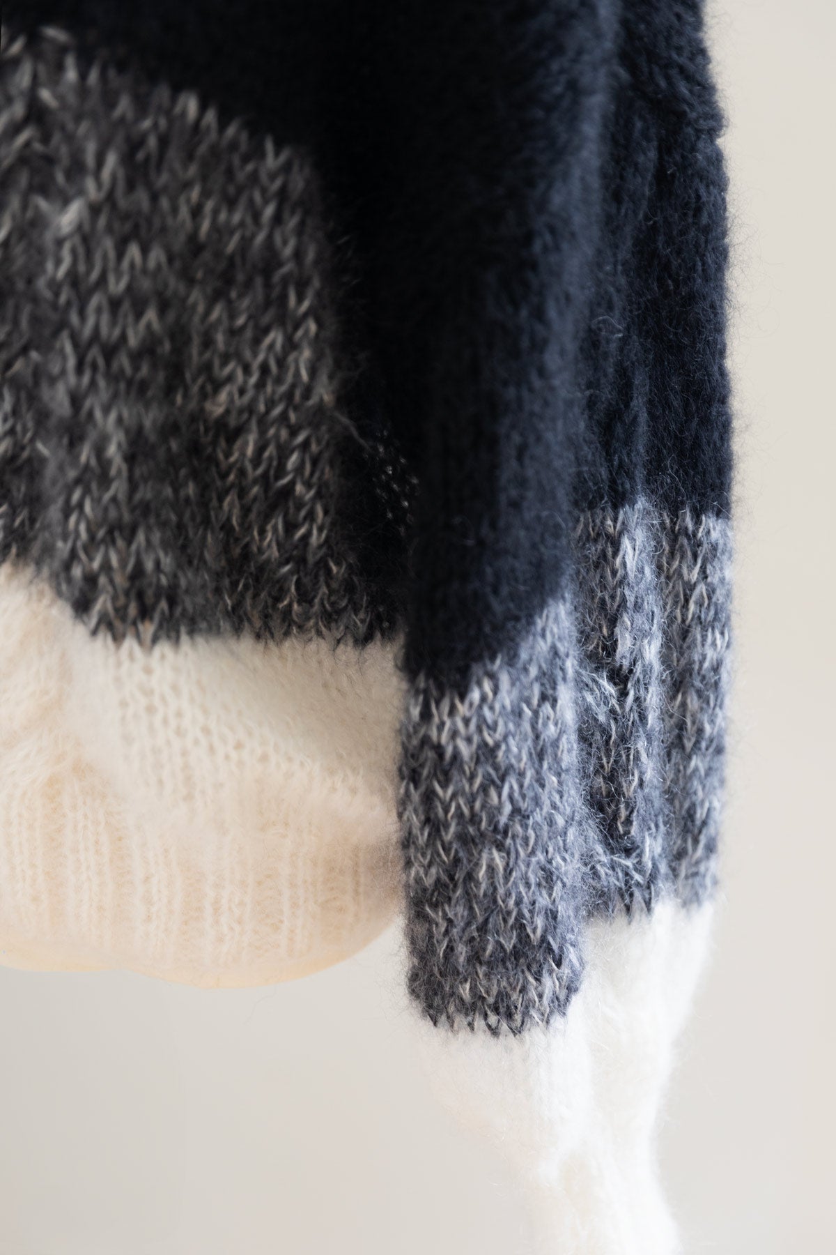 Close-up of a chunky mohair sweater with a colour-blocked pattern featuring black, heather grey, and off-white sections.