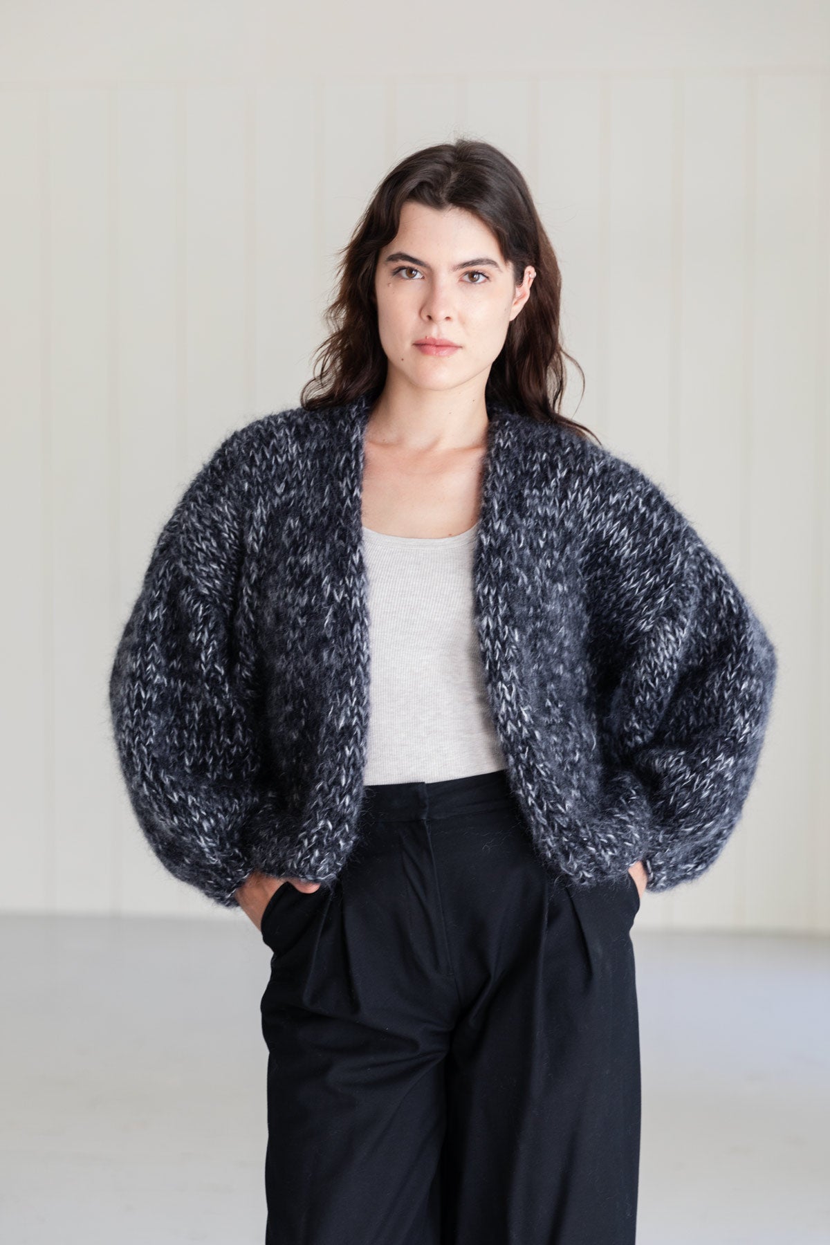 A woman wearing a bomber mohair cardigan in a moulinée black and white pattern, styled over a light grey top and large black pants.