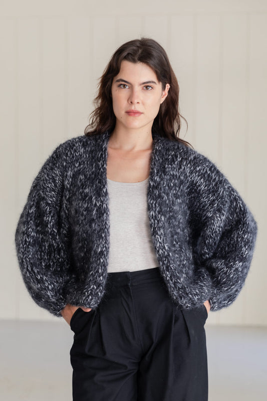 A woman wearing a bomber mohair cardigan in a moulinée black and white pattern, styled over a light grey top and large black pants.