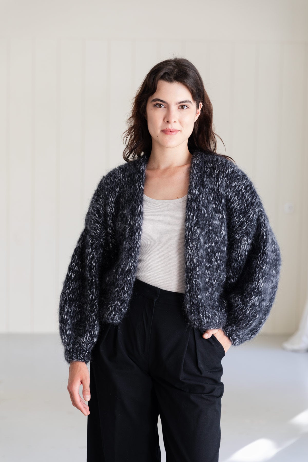 A woman wearing a bomber mohair cardigan in a moulinée black and white pattern, styled over a light grey top and black pants.