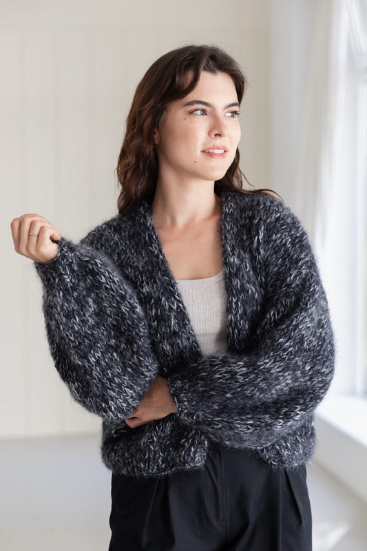 A woman wearing a chunky, mohair cardigan in a moulinée black and white pattern, styled over a light grey top and black pants.