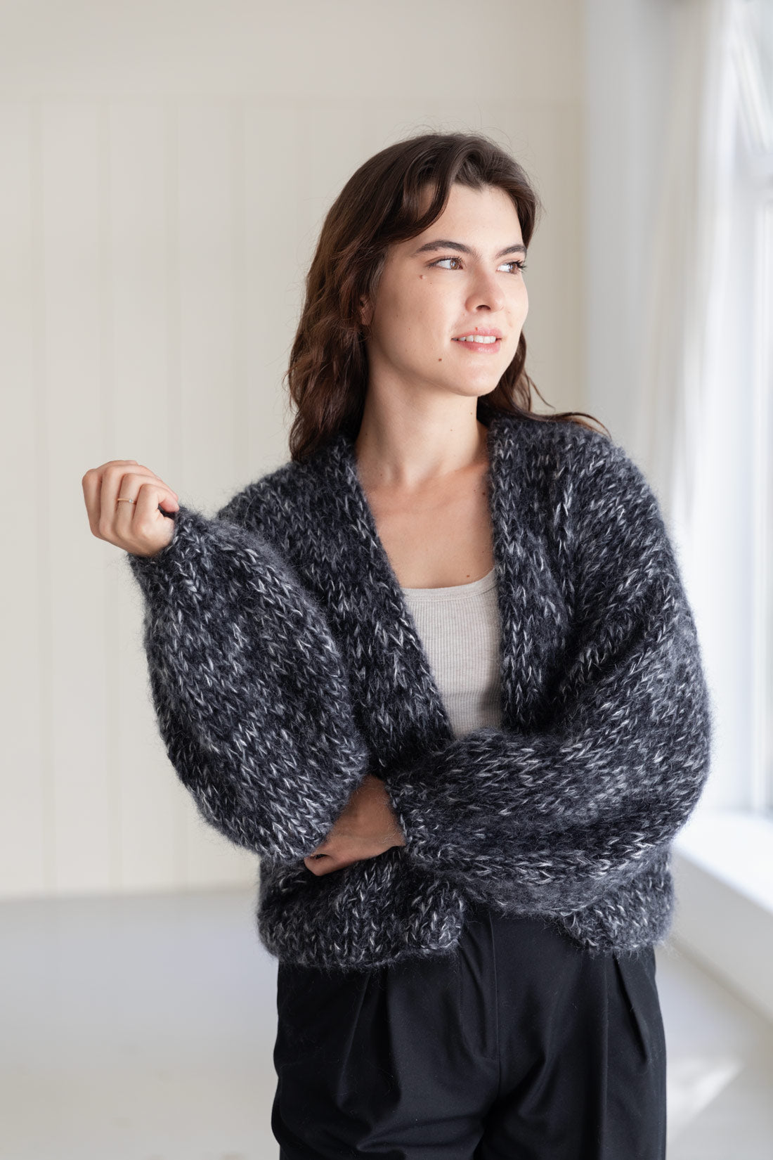 A woman wearing a chunky, mohair cardigan in a moulinée black and white pattern, styled over a light grey top and black pants.