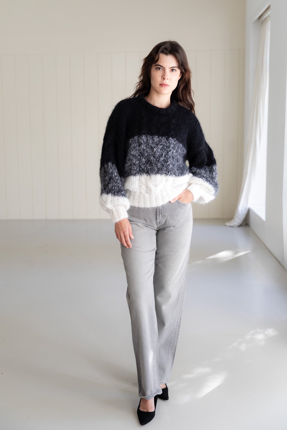 A woman wearing a black and white mohair sweater with puffy sleeves, paired with light grey jeans and black pointed shoes.