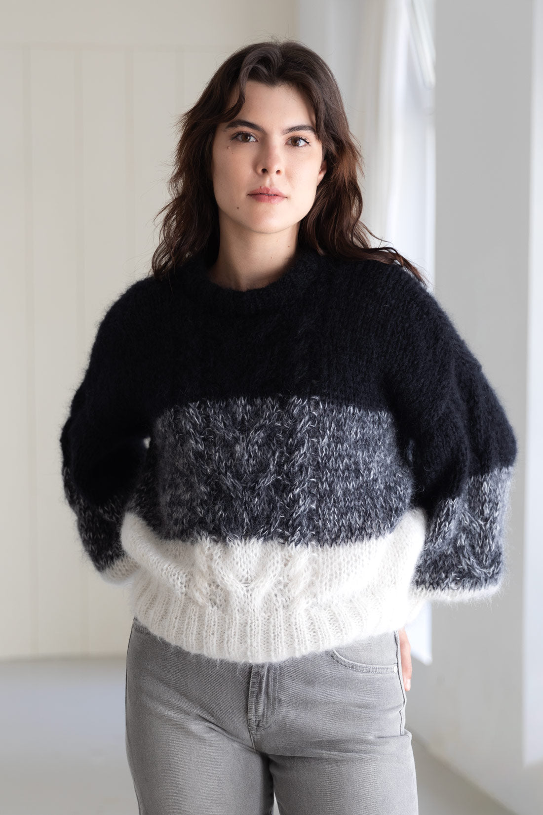 A woman wearing a mohair sweater with a colour-blocked pattern of black, grey, and white, paired with grey denim.