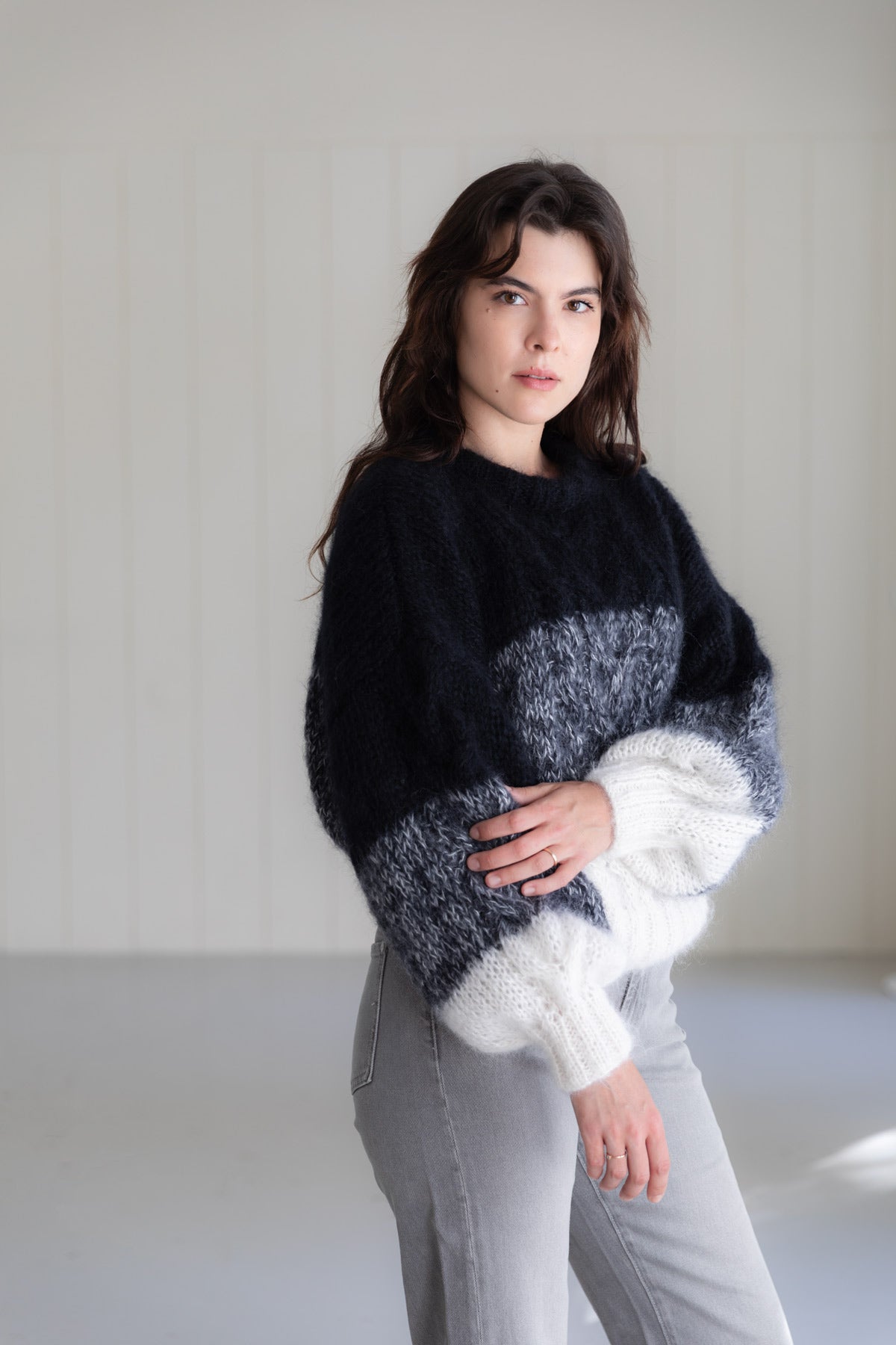 A woman wearing a chunky mohair sweater with a colour-blocked pattern in black, and white, paired with light grey jeans.