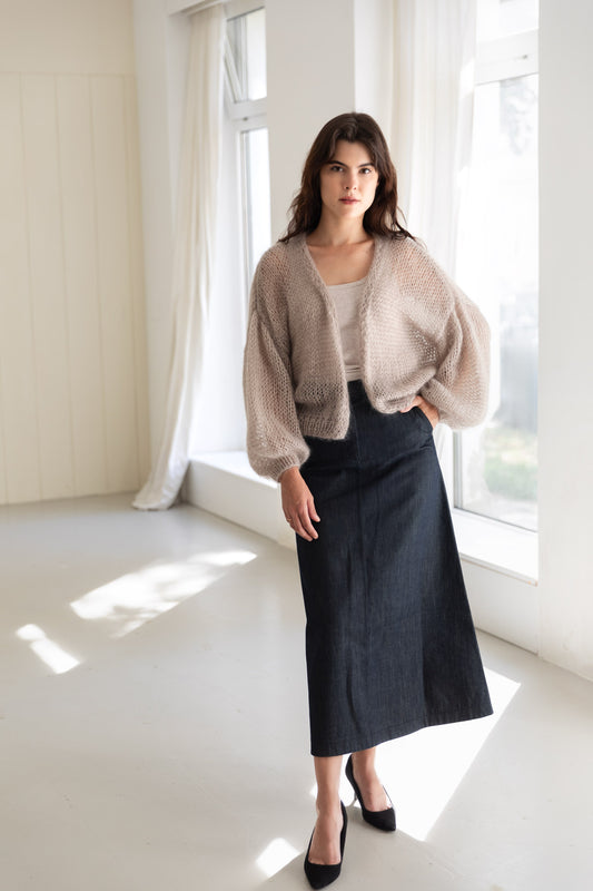 A woman wearing a light beige mohair cardigan over a beige top, paired with a dark navy midi skirt and black pointed shoes.