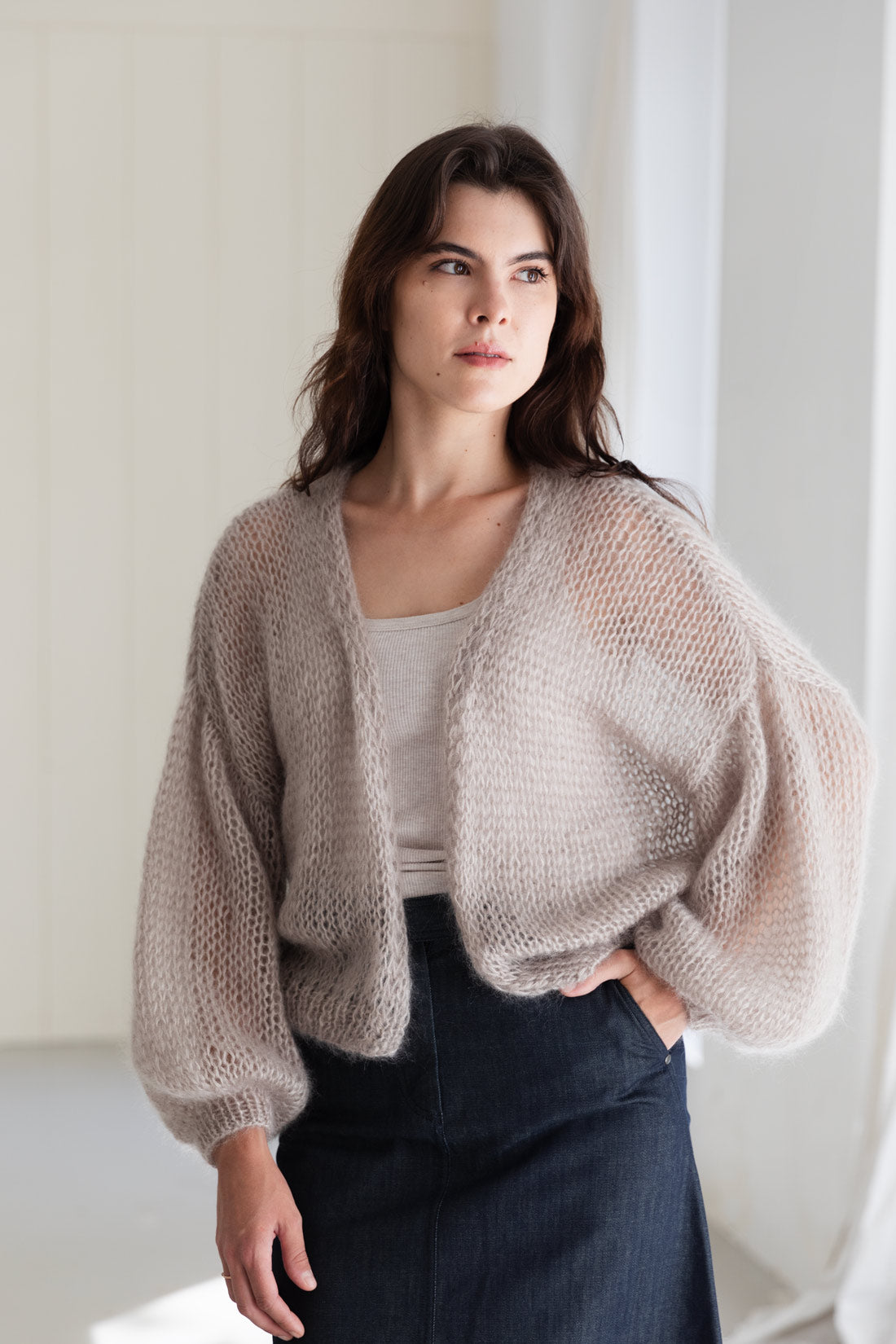 A woman wearing a light beige mohair cardigan over a beige top, paired with a dark denim skirt.