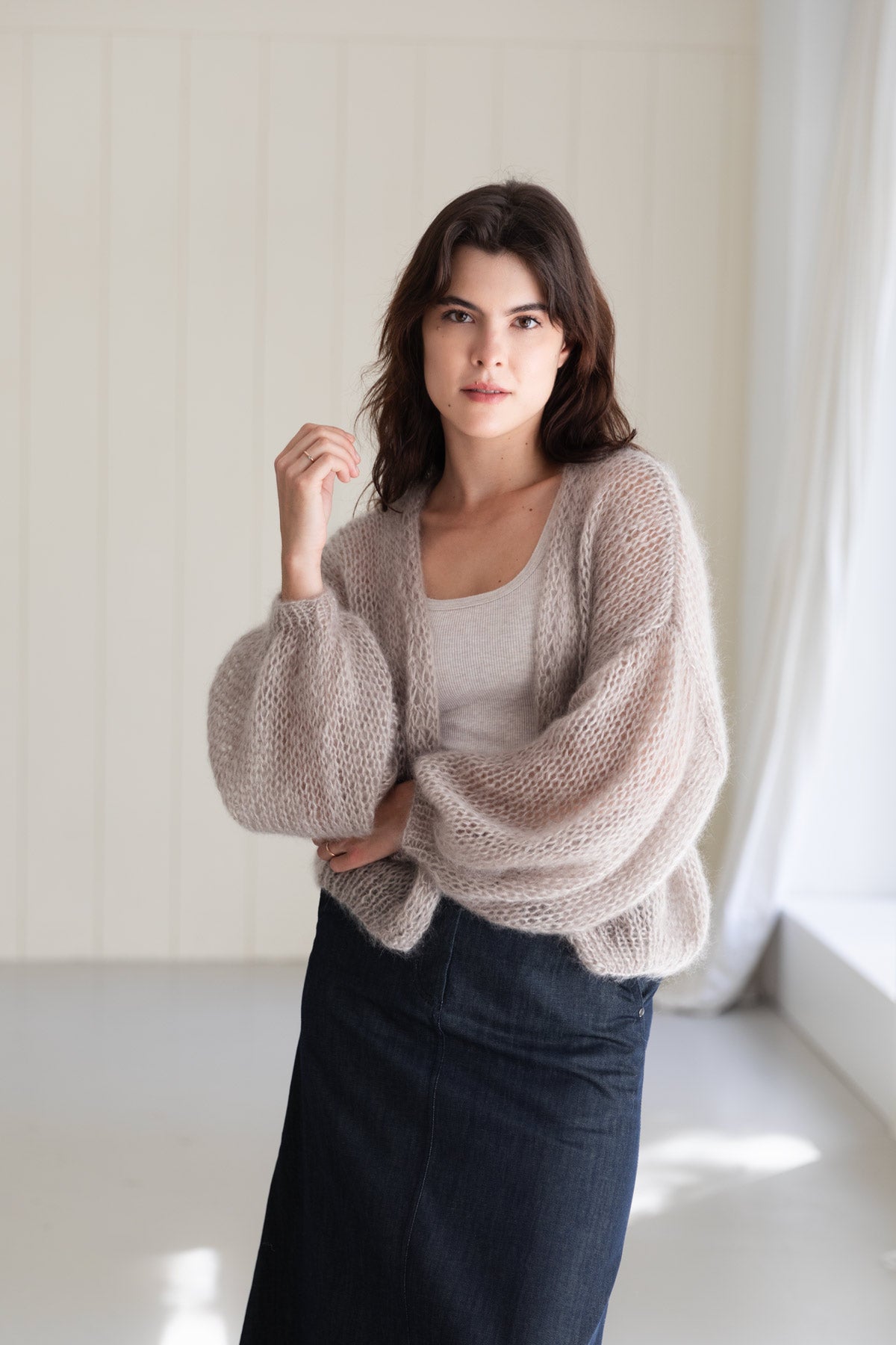 A woman wearing an airy mohair cardigan in a pearl-beige colour, styled over a light top and a dark denim skirt.